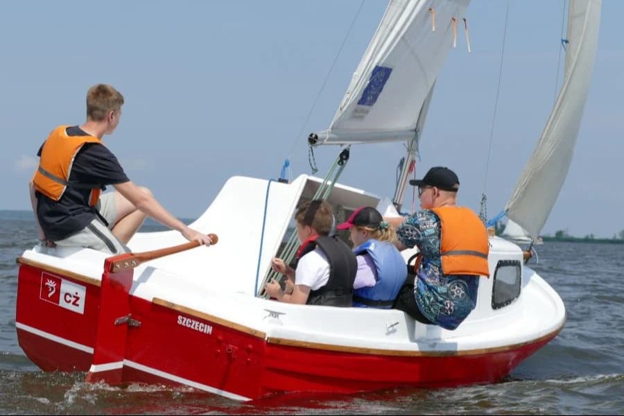Lato pod żaglami. Czas na niezapomnianą przygodę! Młodzi żeglarze na czerwonej łódce,